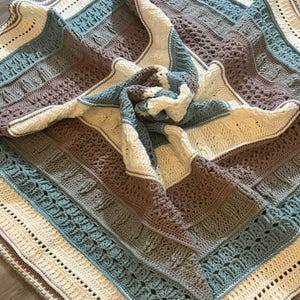 May include: A square crochet blanket featuring a repeating pattern of textured stitches in cream, dusty rose, and muted blue. The design consists of alternating horizontal bands of cable-like textures, openwork, and solid rows, creating a layered effect.