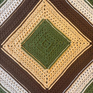 May include: A square crochet blanket featuring a geometric diamond pattern. The design consists of concentric layers in alternating colors of forest green, cream, and dark brown, worked in a textured stitch that creates a repeating diamond motif.