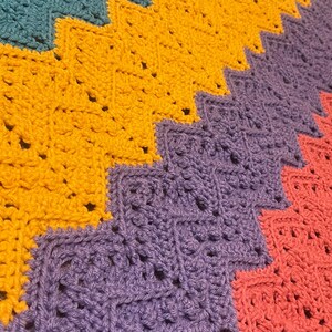 May include: Close-up of a handmade crochet blanket with a zig-zag pattern. The blanket features sections of teal, gold, purple, and coral. The stitches are visible, creating a textured surface. This cozy blanket is perfect for home decor.