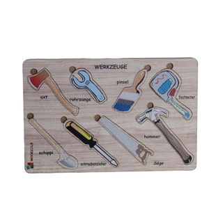 Könnte beinhalten: Holzp Puzzle mit 8 verschiedenen Werkzeugen, darunter eine Axt, eine Zange, ein Pinsel, ein Maßband, ein Hammer, ein Schraubendreher, eine Säge und eine Schaufel. Jedes Werkzeug hat eine deutsche Wortbezeichnung.