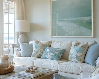 May include: A white couch with blue and white patterned throw pillows in a living room with a large framed seascape painting on the wall. The couch is in front of a coffee table with a book and a piece of driftwood on top.