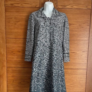 May include: A knee-length dress with a distinctive pattern of grey and white horizontal lines. It has long sleeves with striped cuffs and a collared neckline with a tie. The dress is displayed on a mannequin against a wooden background.
