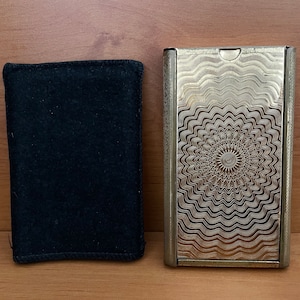May include: Two black rectangular cases, one with a soft fabric cover and the other with a silver metal cover with a decorative pattern.