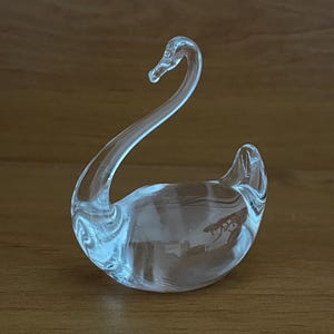 May include: A clear glass swan figurine. The swan has a long neck and a rounded body.