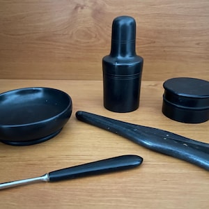 Könnte beinhalten: Ein Set aus vier schwarzen, handgeschnitzten Holzwerkzeugen. Das Set enthält eine kleine Schüssel, einen flaschenförmigen Behälter, eine kleine Box und eine Zange.