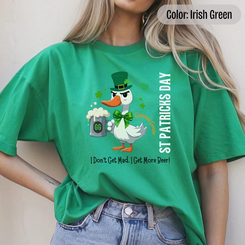 An irish green t-shirt featuring a cartoon goose dressed for St. Patricks Day with a green bow tie, leprechaun hat, and shamrocks. The goose, named Guinness Goose, holds a frothy beer mug labeled GG with a playful, mischievous expression. Surrounding elements include shamrocks. The words ST PATRICKS DAY are written vertically on the right, with the words I Dont Get Mad I Get More Beer!, are written horizontally below.