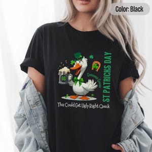 A black t-shirt featuring a cartoon goose dressed for St. Patricks Day with a green bow tie, leprechaun hat, and shamrocks. The goose, named Guinness Goose, holds a frothy beer mug labeled GG with a playful, mischievous expression. Surrounding elements include a horseshoe and festive decorations. The words ST PATRICKS DAY are written vertically on the right, with the words This Could Get Ugly Right Quick is written horizontally below.