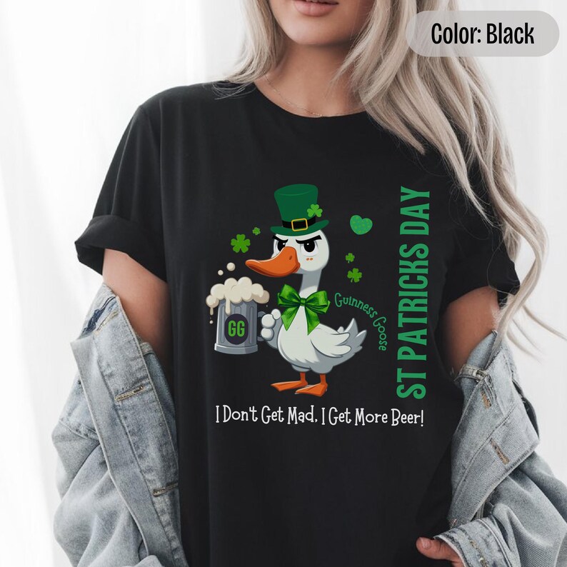A blak t-shirt featuring a cartoon goose dressed for St. Patricks Day with a green bow tie, leprechaun hat, and shamrocks. The goose, named Guinness Goose, holds a frothy beer mug labeled GG with a playful, mischievous expression. Surrounding elements include shamrocks. The words ST PATRICKS DAY are written vertically on the right, with the words I Dont Get Mad I Get More Beer!, are written horizontally below.