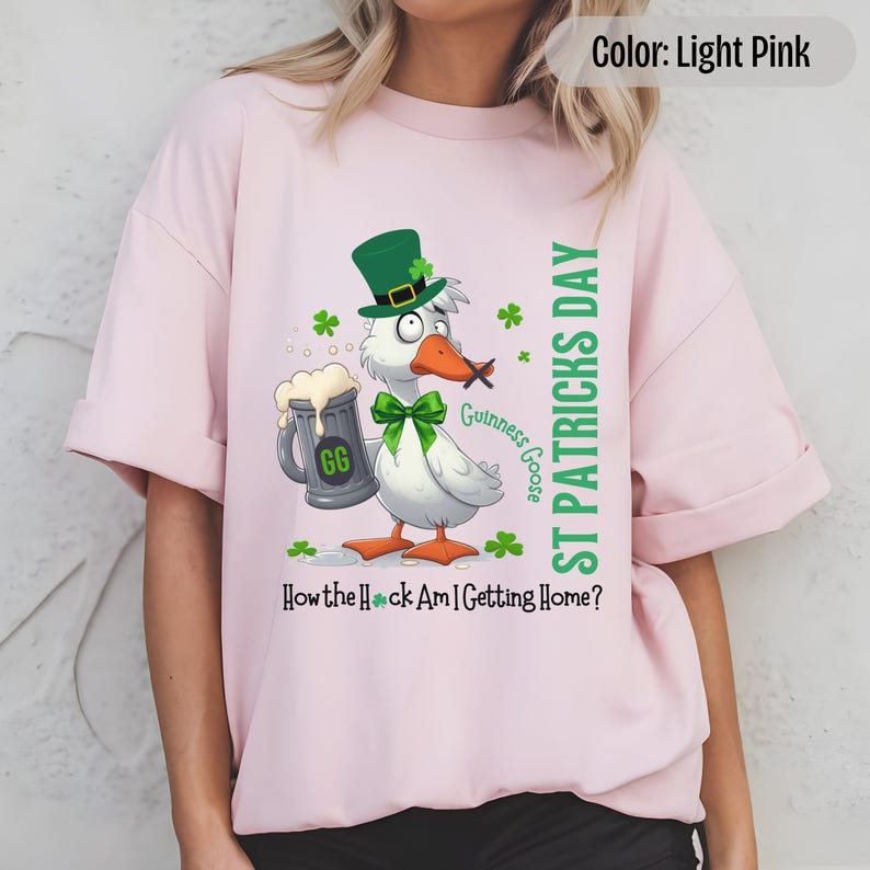 A light pink t-shirt featuring a cartoon goose dressed for St. Patricks Day with a green bow tie, leprechaun hat, and shamrocks. The goose, named Guinness Goose, holds a frothy beer mug labeled GG with a playful, mischievous expression. Surrounding elements include shamrocks. The words ST PATRICKS DAY are written vertically on the right, with the words How the Heck Am I Getting Home? are written horizontally below.