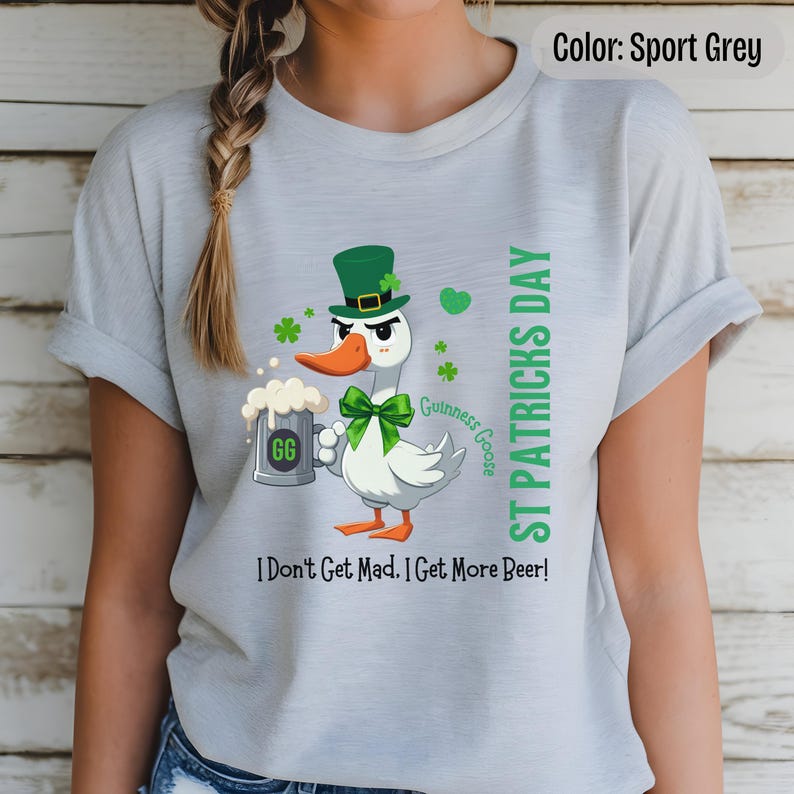 A sport grey t-shirt featuring a cartoon goose dressed for St. Patricks Day with a green bow tie, leprechaun hat, and shamrocks. The goose, named Guinness Goose, holds a frothy beer mug labeled GG with a playful, mischievous expression. Surrounding elements include shamrocks. The words ST PATRICKS DAY are written vertically on the right, with the words I Dont Get Mad I Get More Beer!, are written horizontally below.