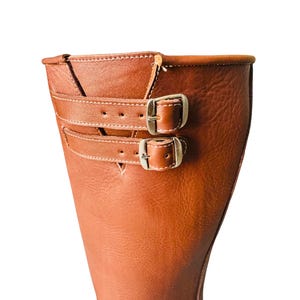 May include: Close-up of the top of a brown leather boot with two silver buckles.