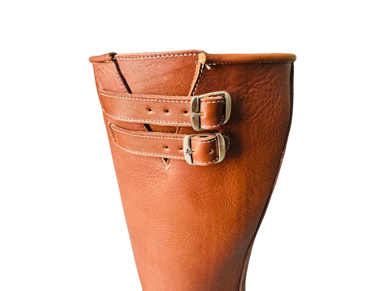 May include: Close-up of the top of a brown leather boot with two silver buckles.