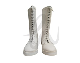 Pode incluir: Um par de botas de luta livre de couro branco com cadarços. As botas são altas e têm uma ponta arredondada.