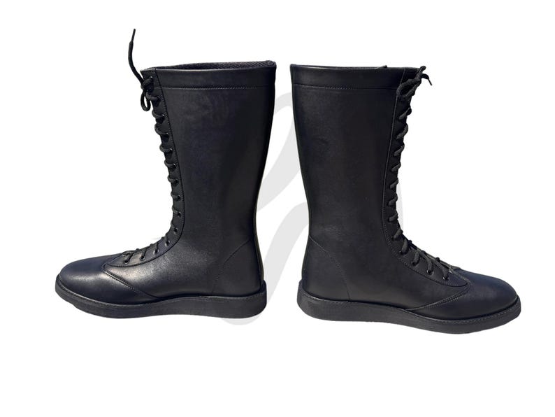 Puede incluir: Un par de botas de lucha libre de cuero negro con cordones en la parte delantera. Las botas tienen una suela plana.