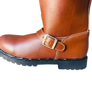 May include: Brown leather motorcycle boots with a buckle closure and a black rubber sole.