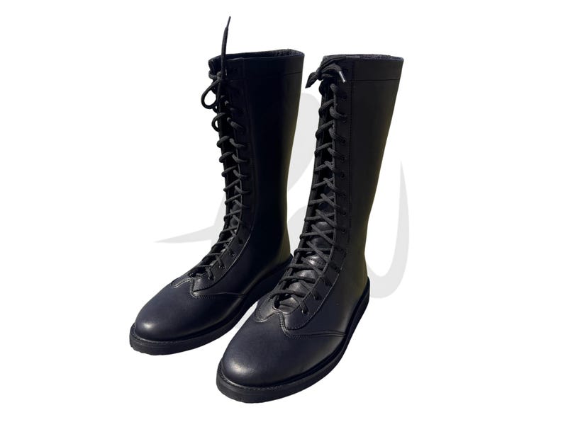 Puede incluir: Un par de botas de lucha libre de cuero negro con cordones. Las botas tienen una ca&ntilde;a alta y una suela gruesa.