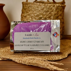 Puede incluir: Un paquete de baño de burbujas efervescente de lavanda. La etiqueta dice "Lavish 4 Less" y contiene el texto "Bergamota y Lavanda Baño de Burbujas Efervescente". El paquete contiene 60 g de producto.