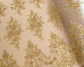 May include: A roll of beige tulle fabric featuring an intricate gold embroidery pattern with floral motifs, metallic thread, and small sequins. The fabric displays the text Secret Spark Fabrics and includes a scalloped edge with detailed gold stitching.