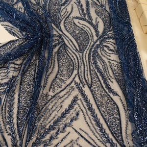 May include: Navy blue beaded fabric with an intricate, organic pattern. The design features flowing lines and leaf-like shapes, all embellished with shimmering beads. The fabric is semi-transparent, revealing a neutral background. The text "SECRET SPARK" is visible.