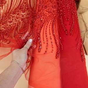 Könnte beinhalten: Leuchtend roter Stoff mit aufwendigen Perlen- und Paillettenverzierungen. Der Stoff hat ein transparentes, mehrschichtiges Aussehen. Der Text "SECRET SPARK fabrics" ist oben rechts sichtbar.