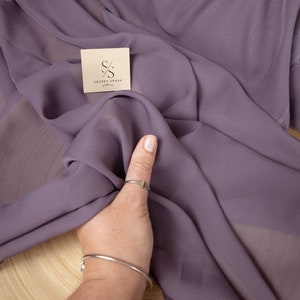 May include: A close-up of a soft, purple fabric with a textured surface. The fabric is draped over a wooden surface. The text "SECRET SPARK fabrics" is visible on the fabric.