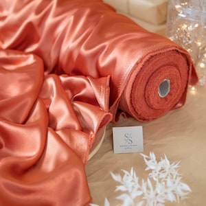 May include: A roll of burnt orange satin fabric with a white tag that says "Secret Spark Fabrics".