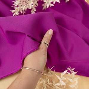 Puede incluir: Primer plano de una mano con un anillo de plata que dice "love" en el pulgar. La mano está sosteniendo un trozo de tela magenta brillante.