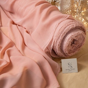 May include: A roll of pale pink chiffon fabric with a frayed edge. The fabric is rolled up and sitting on a brown surface. The text "SECRET SPARK fabrics" is visible on a small tag.