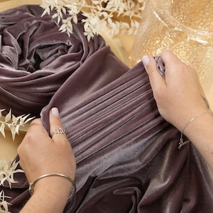 May include: A close-up of a soft, mauve velvet fabric being held by a hand. The fabric is folded and has a subtle sheen. The text "SECRET SPARK" is visible in the top left corner of the image.