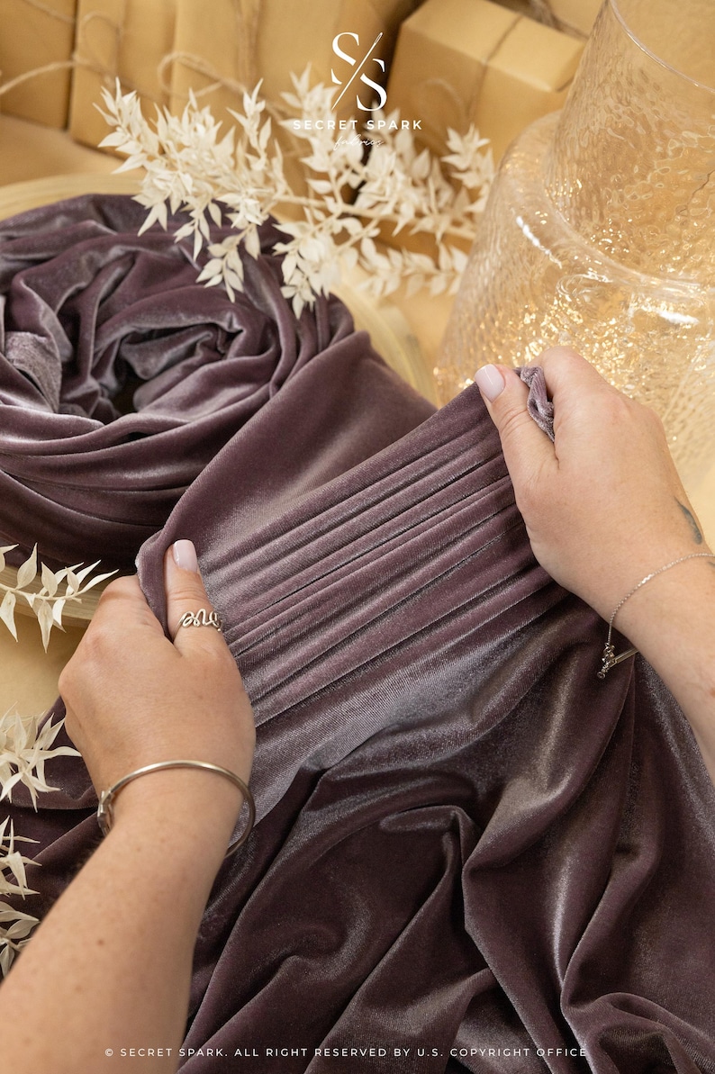 May include: A close-up of a soft, mauve velvet fabric being held by a hand. The fabric is folded and has a subtle sheen. The text "SECRET SPARK" is visible in the top left corner of the image.