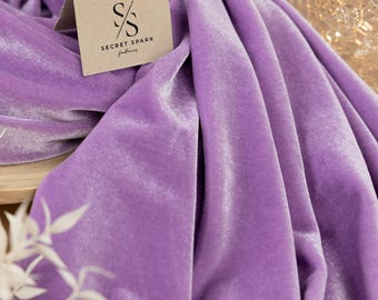 May include: A close-up of a soft, purple velvet fabric. The fabric is draped over a wooden surface and has a subtle sheen. The fabric is labeled "SECRET SPARK fabrics".