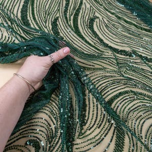 May include: Dark green beaded fabric with a wave-like pattern. The fabric is held up, showing the intricate beadwork and the sheer backing. The text "SECRET SPARK fabrics" is visible.