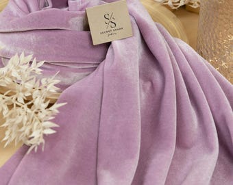May include: A soft, lilac velvet fabric with a subtle sheen. The fabric is folded and draped on a wooden surface. The Secret Spark Fabrics logo is visible on a small tag.