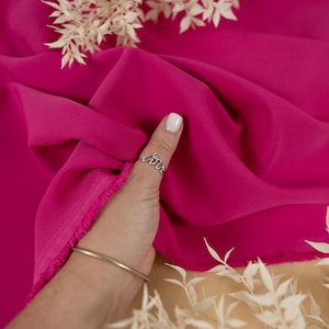 May include: A close-up of a bright pink fabric with a hand holding a ring that says "love". The fabric is smooth and silky.