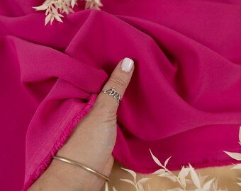 May include: A close-up of a bright pink fabric with a hand holding a ring that says "love". The fabric is smooth and silky.