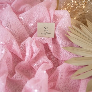 May include: Pink sequin fabric with a brown tag that says "SECRET SPARK fabrics".