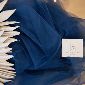 May include: A close-up of a navy blue tulle fabric with a white tag that says "SECRET SPARK fabrics".