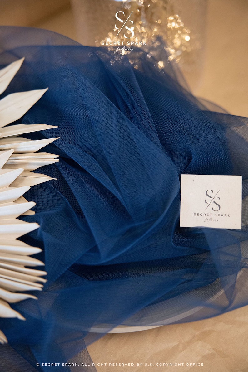May include: A close-up of a navy blue tulle fabric with a white tag that says "SECRET SPARK fabrics".