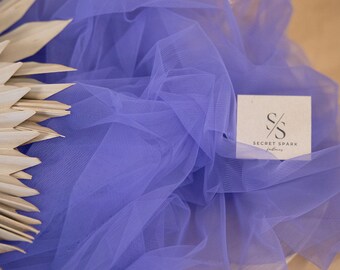 May include: A close-up of a purple tulle fabric with the text "SECRET SPARK fabrics" on a white tag. The fabric is soft and delicate, perfect for crafting and DIY projects.