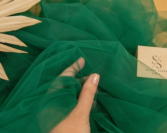 Może przedstawiać: Zbliżenie na jasnozielony tiul. Tkanina jest miękka i przezroczysta, o delikatnej fakturze. Tkanina jest trzymana przez dłoń, a tło jest rozmyte.