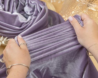 May include: A soft, lilac velvet fabric is being held and folded by a hand. The fabric is smooth and has a subtle sheen. The fabric is perfect for crafting, sewing, or home decor projects.