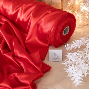 Peut inclure: Un rouleau de tissu satiné rouge vif avec un bord frangé. Le tissu est enroulé et posé sur une surface brune. Le tissu est de Secret Spark Fabrics.