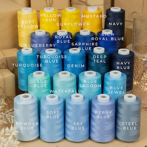 May include: A collection of spools of thread in various shades of blue and yellow. The spools are arranged in rows, with the colours transitioning from yellow to blue. The spools are labelled with the names of the colours, such as "Soft Yellow", "Royal Blue", and "Deep Teal".