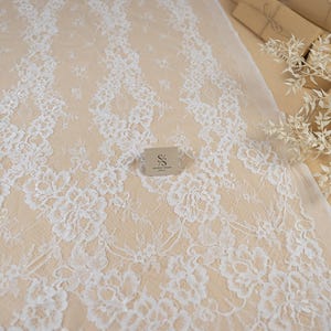 May include: White floral lace fabric with a delicate pattern. The lace is laid out on a beige surface. The image includes the text "SECRET SPARK fabrics" and "SECRET SPARK. ALL RIGHT RESERVED BY U.S. COPYRIGHT OFFICE."