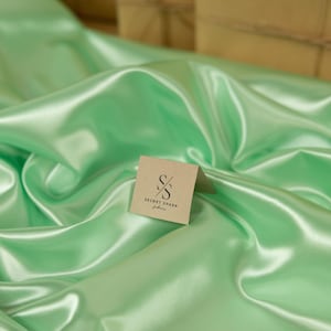 May include: A light green satin fabric with a brown tag that says "SECRET SPARK fabrics" on it.