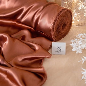 May include: A roll of rust-colored satin fabric with a label that reads "Secret Spark Fabrics".