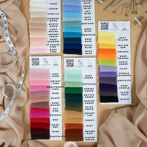 K&ouml;nnte beinhalten: Eine Farbkarte mit Stoffproben aus 100 % Polyester-Chiffon in verschiedenen Farben, darunter Wei&szlig;, Grau, Blau, Gelb, Gr&uuml;n, Rosa, Rot, Braun und Schwarz. Der Stoff wird als weich, luftig und matt beschrieben. Der Text "Aura Soft, Airy & Matte Chiffon Fabric" ist oben auf der Karte abgebildet.