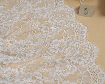 May include: Close-up of white floral lace fabric, showcasing a detailed pattern. The lace is laid on a beige surface. The image includes the "SECRET SPARK" logo. The fabric's intricate design and texture are highlighted.