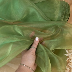 May include: Green sheer fabric with a subtle shimmer. The fabric is folded and held in a hand. The text "SECRET SPARK fabrics" is visible in the top center of the image.
