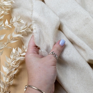 May include: A piece of off-white, textured fabric with visible flecks and a raw, frayed edge. The fabric is draped in soft folds. A logo at the top reads SECRET SPARK fabrics, and text at the bottom reads SECRET SPARK. ALL RIGHT RESERVED BY U.S. COPYRIGHT OFFICE.